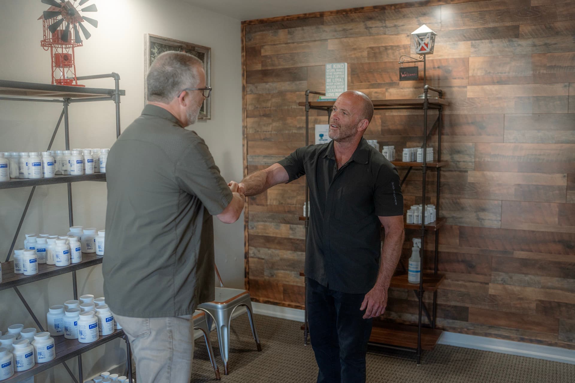 Mark shaking hands with a patient beside the clinic supplement shelves